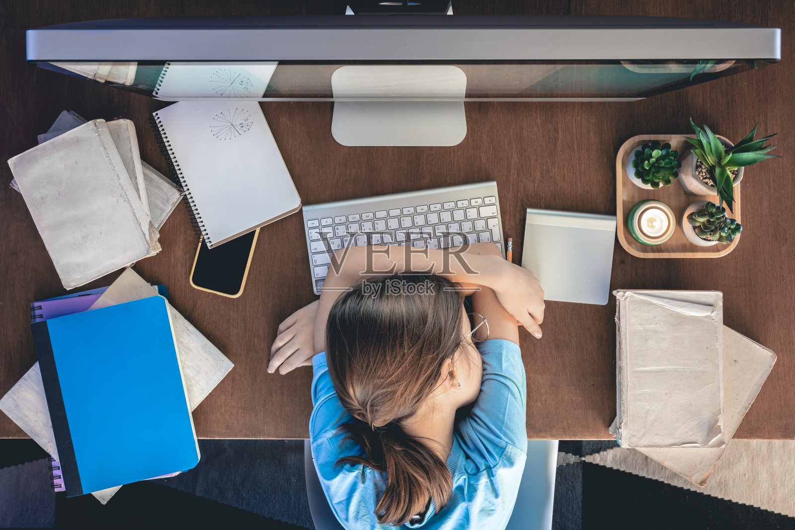 一个疲惫的女孩躺在电脑前的桌子上，桌上放着笔记本和书。照片摄影图片