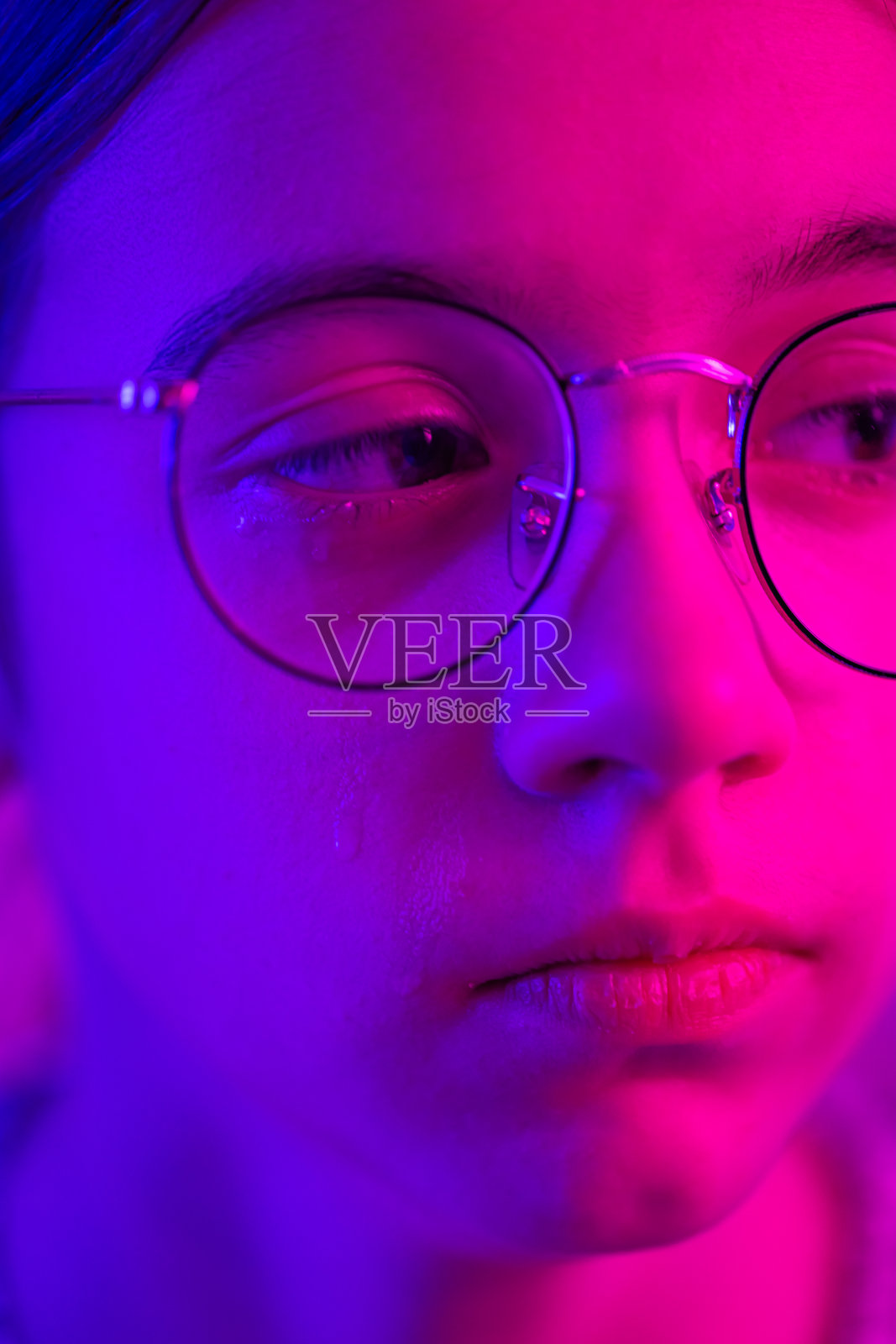 戴眼镜的可爱女孩在霓虹灯下哭泣，脸部特写。照片摄影图片