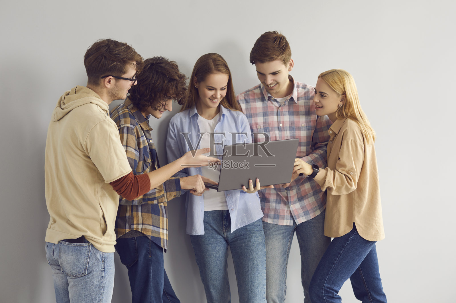 快乐的少女向微笑的青少年朋友展示笔记本电脑照片摄影图片