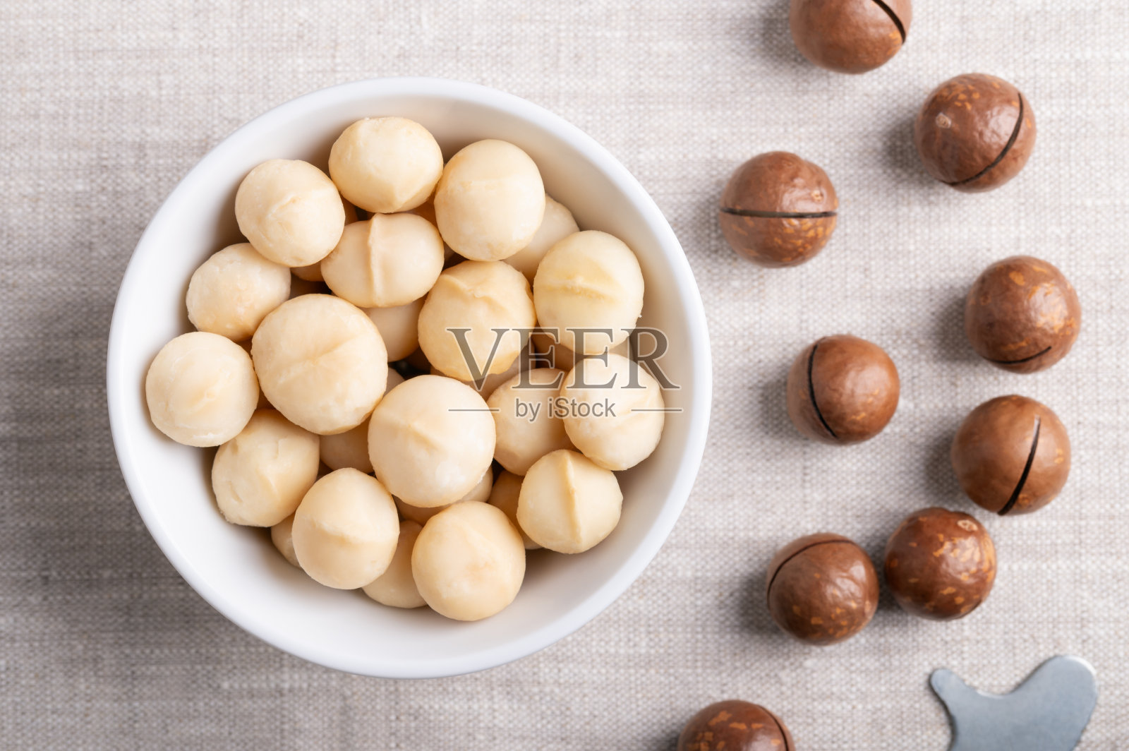 在亚麻织物上的白色碗里烤夏威夷坚果照片摄影图片