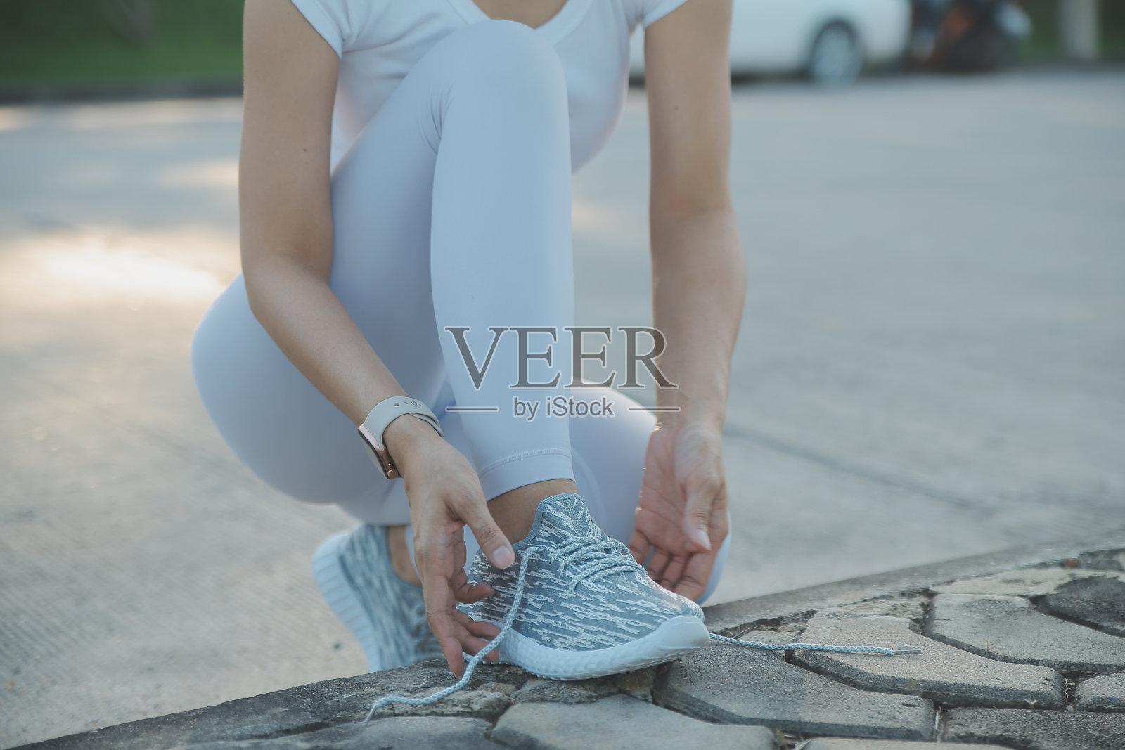 成熟的健身女人在路上系鞋带。穿着运动鞋，带着手机和耳机坐在城市街道的地板上。活跃的拉丁妇女在跑步前系鞋带。照片摄影图片