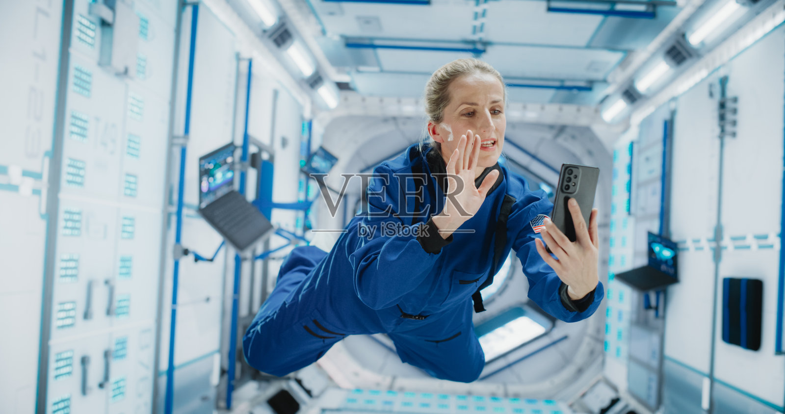 在零重力的卫星上飞行时，在太空中打电话的女人。宇航员通过智能手机上的视频通话应用程序与任务控制中心、家里的家人或同事聊天。照片摄影图片