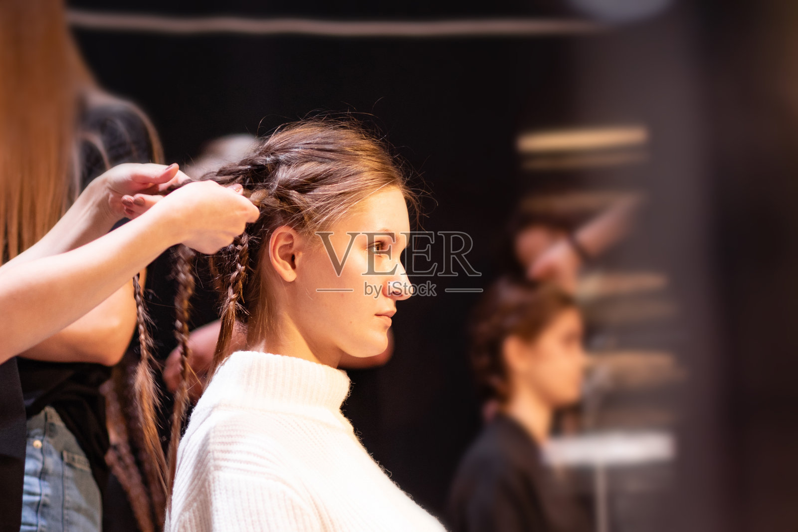 时装周的幕后秀。一个专业的模特在后台。年轻女性在t台附近工作。和漂亮的人合影。准备发型和化妆的女士。照片摄影图片