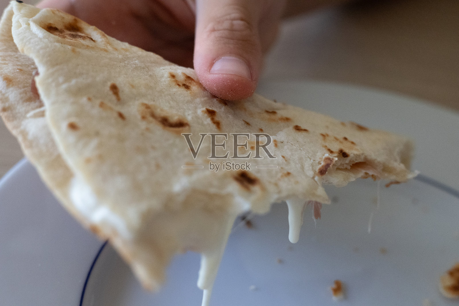 手拿着被咬过的扁平面包，夹着奶酪和火腿放在盘子上照片摄影图片