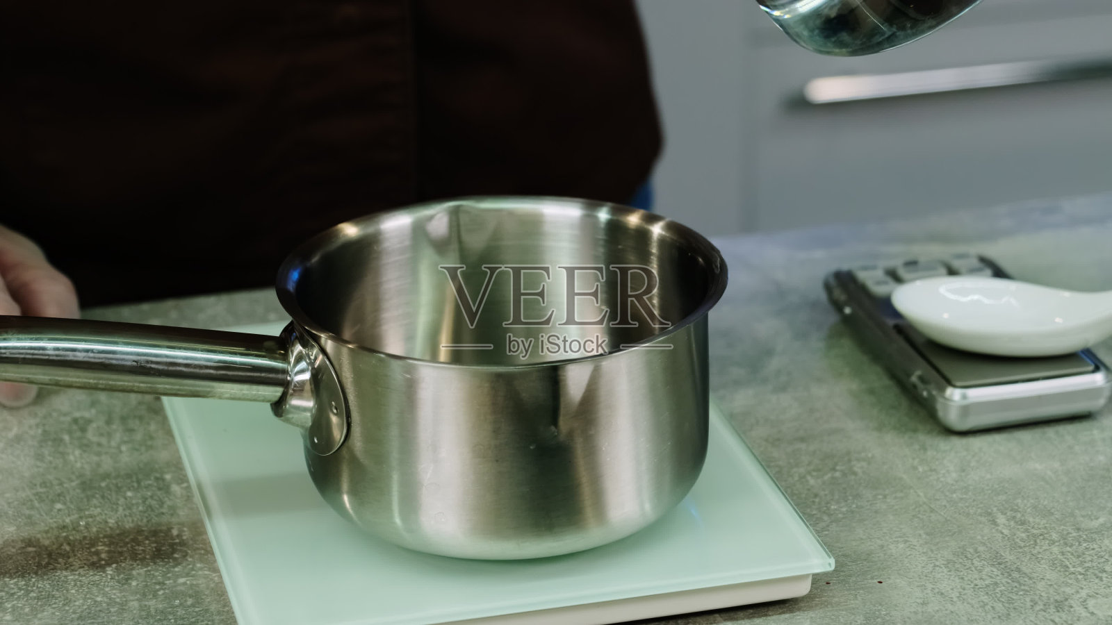 男子将量杯里的水倒入称上的炖锅照片摄影图片