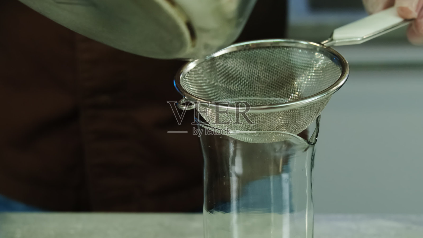 男子通过筛子将混合液体倒入玻璃杯中照片摄影图片
