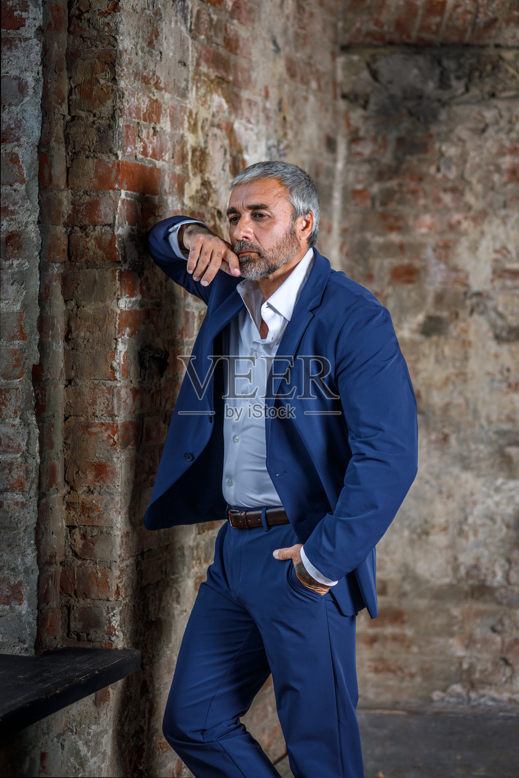 一位身穿蓝色正装的英俊中年男子在灰色背景上摆姿势。一个商人的肖像。一个英俊的中年男子在灰色背景上摆姿势，有一个地方可以复制照片摄影图片