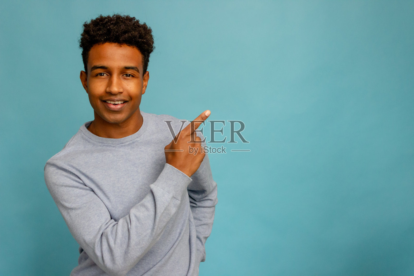 年轻的非裔美国男人在蓝色背景中用手指指向空白处照片摄影图片