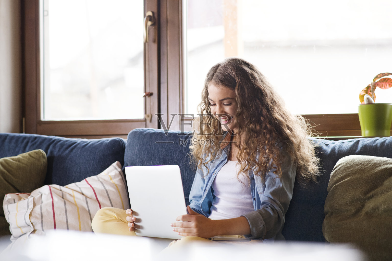 一个漂亮的大学生在网上上课，网上学习坐在家里的沙发上，膝上放着笔记本电脑。照片摄影图片