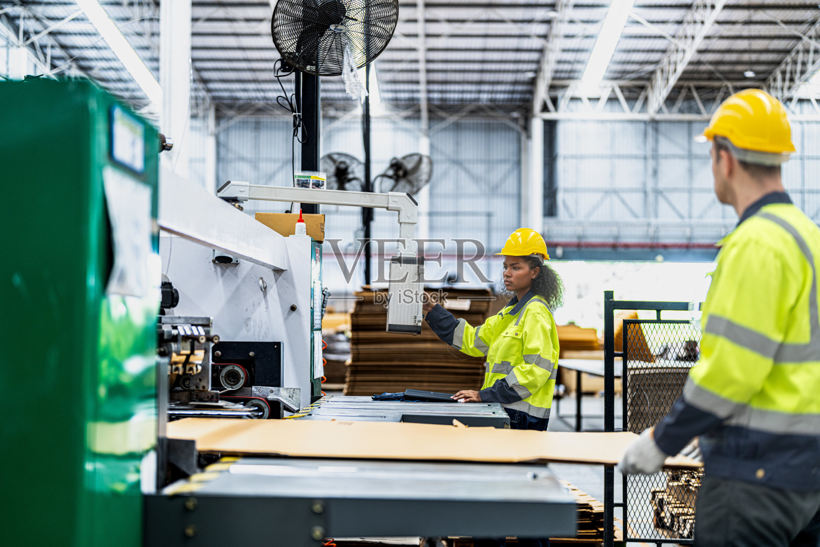 男女技术人员在重型机上检查工艺。机械工程队生产。工业制造业。工人拿着药片和文件夹。高科技生产。照片摄影图片