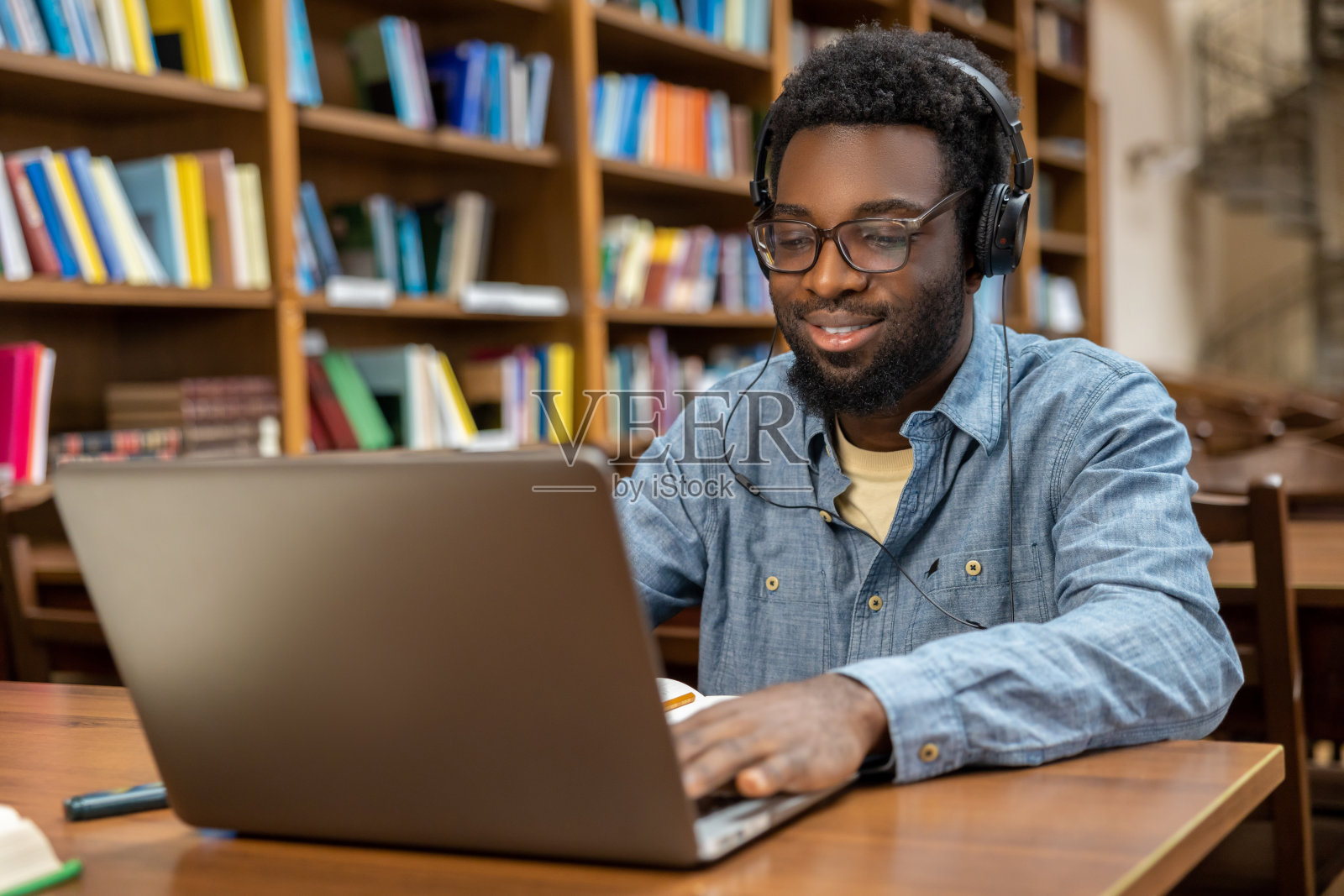 一个戴着耳机在笔记本电脑上工作的非裔美国年轻人照片摄影图片