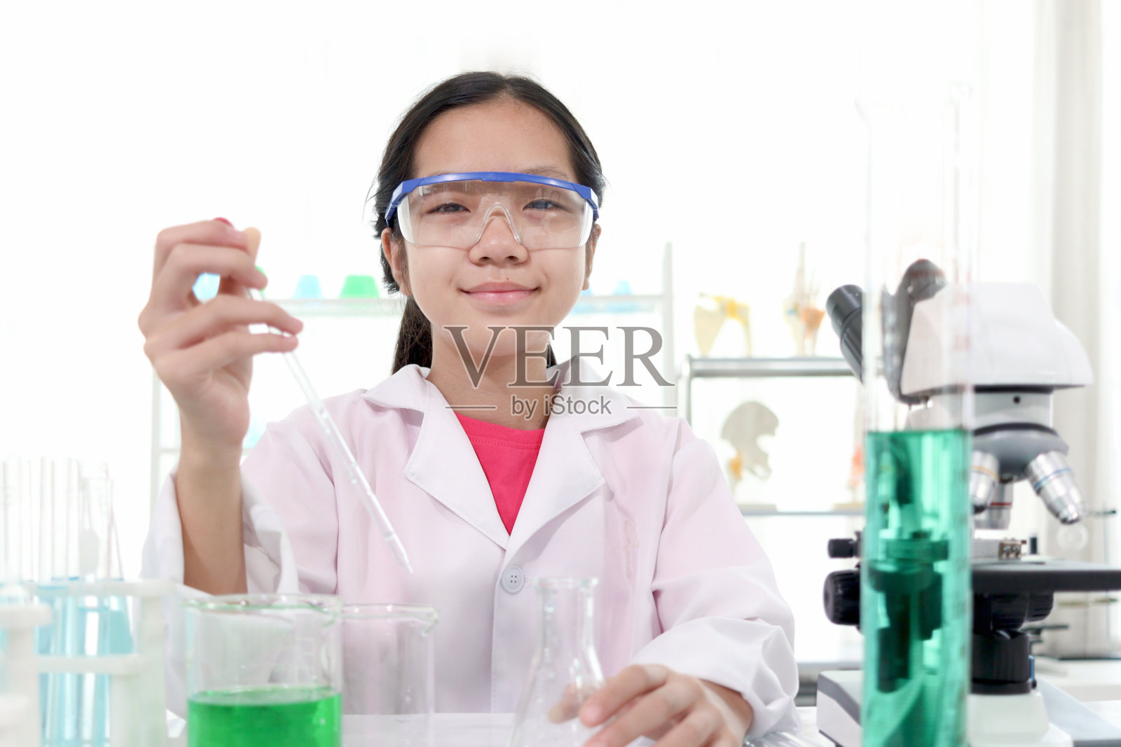 可爱的年轻女科学家穿着实验服，戴着安全眼镜，做着科学实验。快乐的女学生在实验室学习化学的肖像。孩子学习科学教育。照片摄影图片