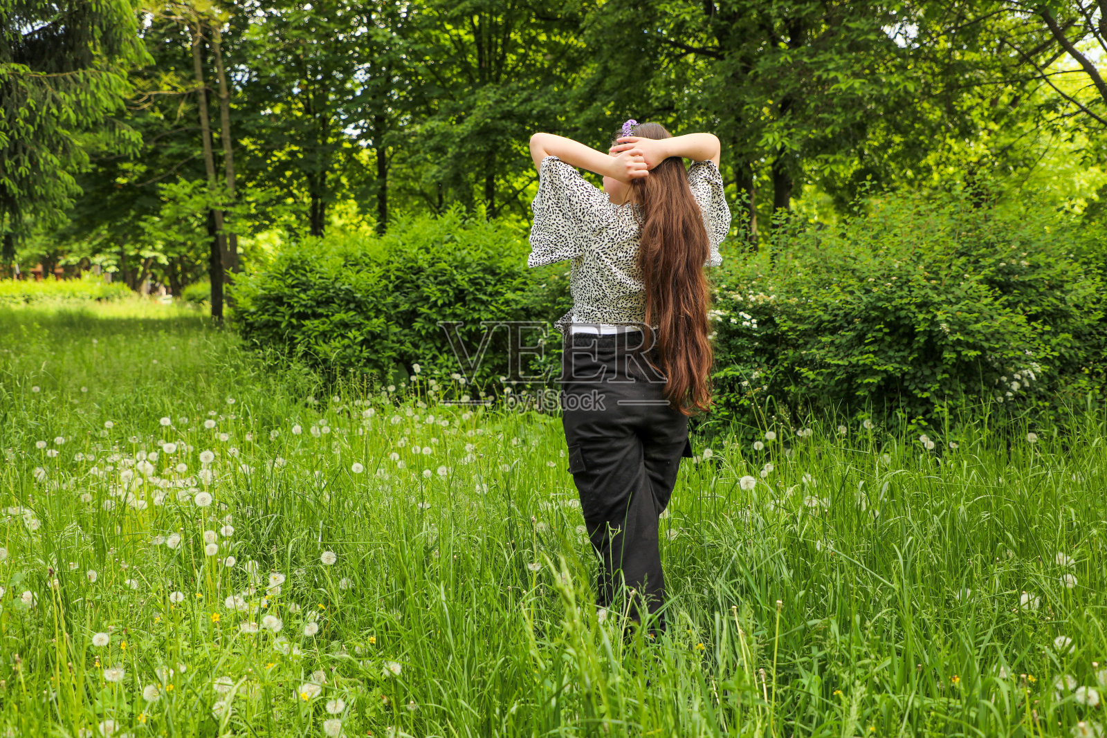一个穿着裤子的年轻女孩站在高高的草丛中，拉直她的长发。照片摄影图片