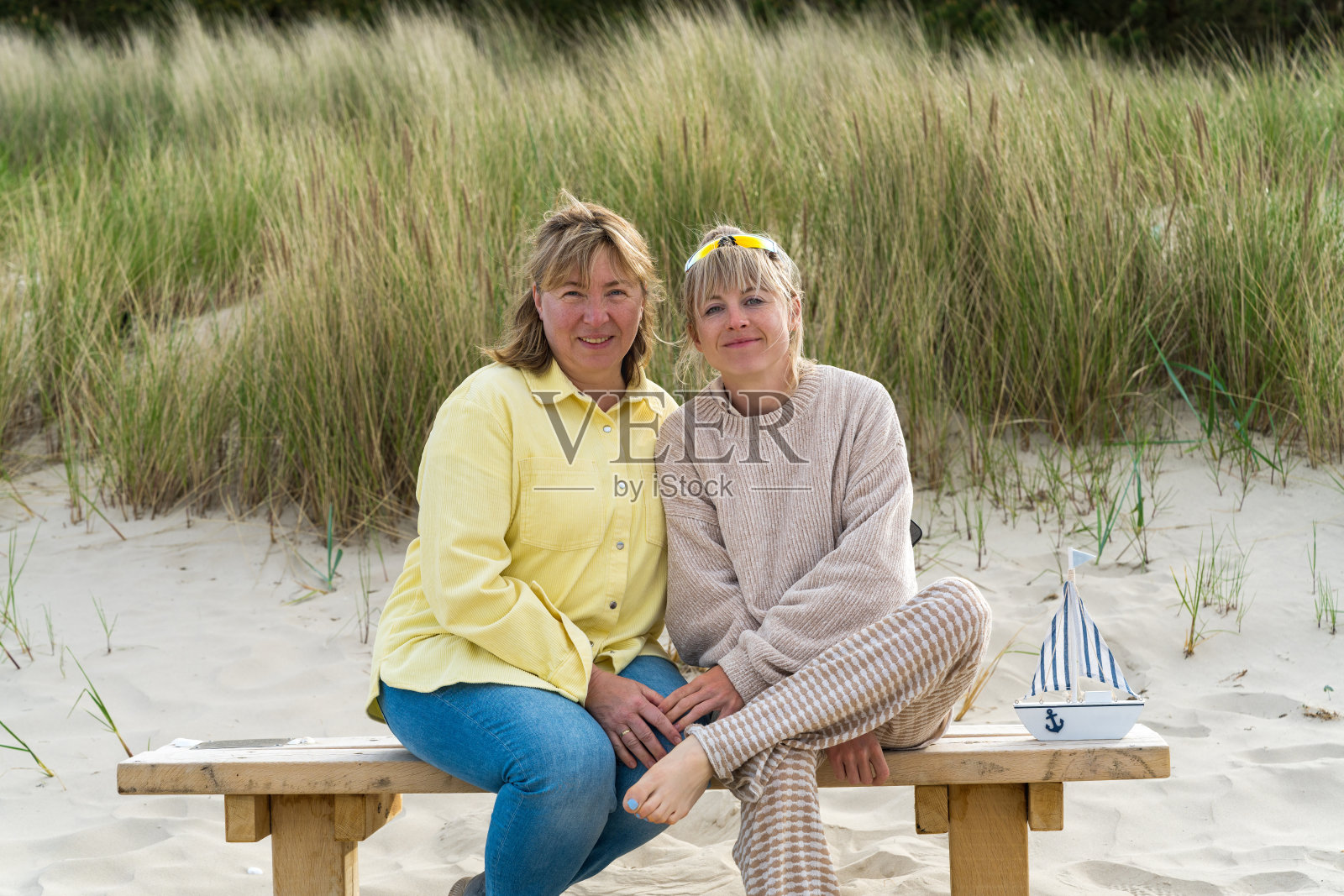 一位母亲带着已成年的女儿在海上的画像。一个女人和一个女孩坐在沙滩上的长椅上，身后是沙丘。波罗的海，沙丘。家庭度假。照片摄影图片