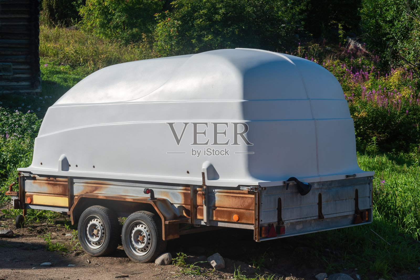 一辆盖着塑料盖的汽车拖车，停在一条河和一片森林旁边的一个未经铺设的停车场里。照片摄影图片