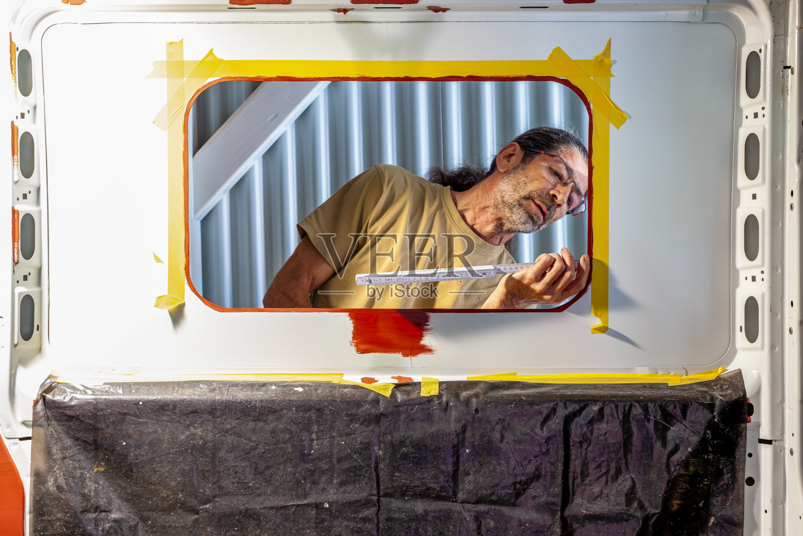 测量窗口。露营车改装-男子安装侧窗。在一辆露营车内，一名男工人正在测量侧窗照片摄影图片