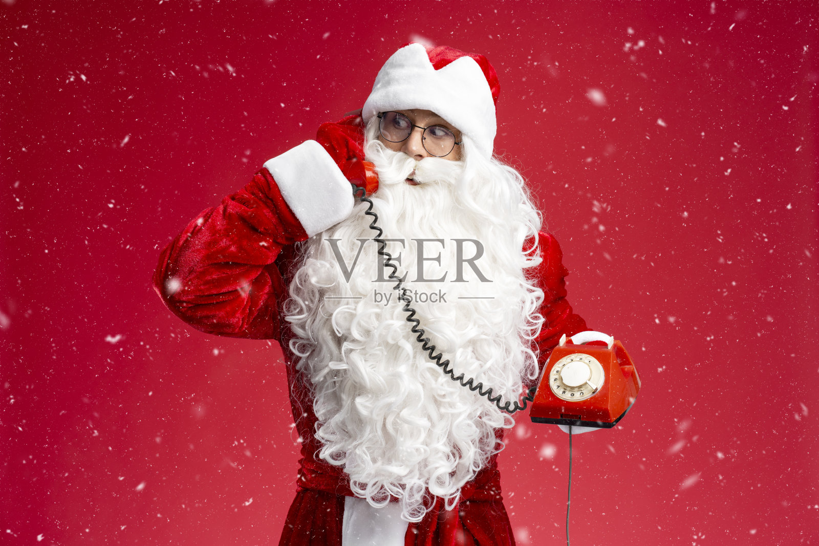 圣诞老人拿着复古的电话接听电话，听着祝福语隔着红色的背景。照片摄影图片