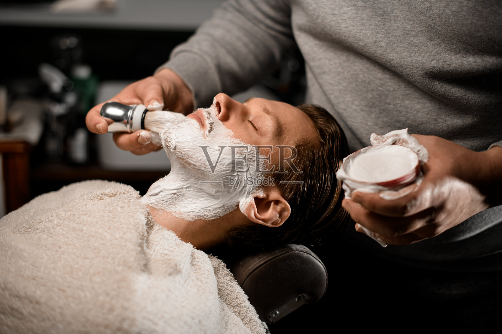 理发师在理发店剃须前将剃须膏涂在顾客的胡须上照片摄影图片