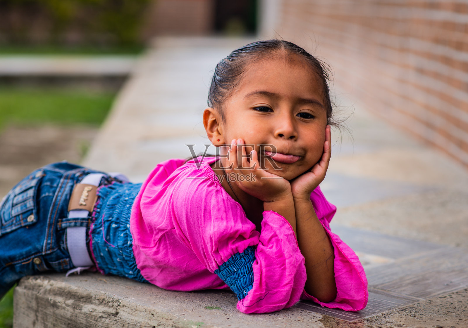 一个小女孩的肖像，非常放松，她的手放在她的脸上，在户外的地面照片摄影图片