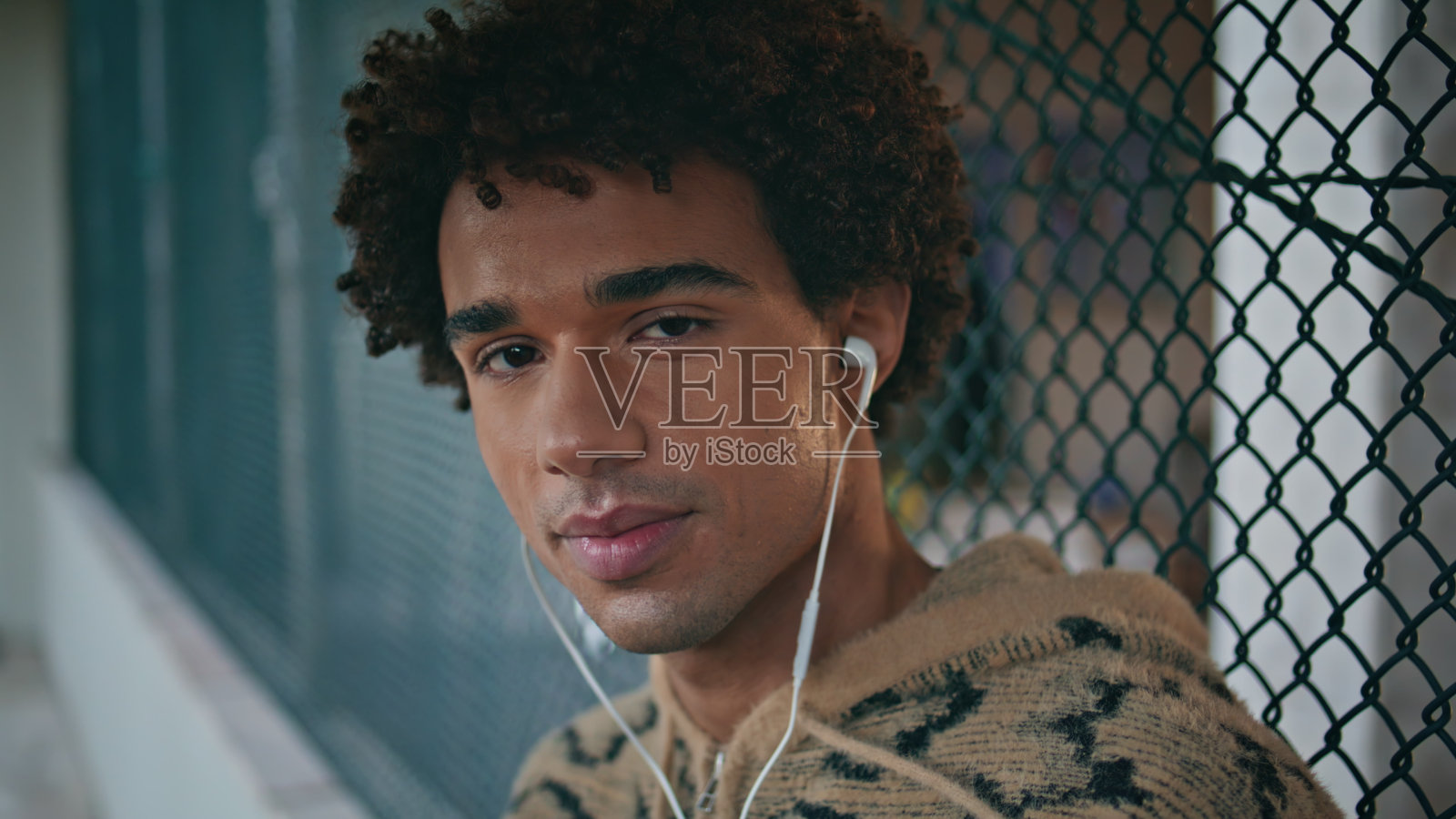 戴着耳机的家伙微笑着看着镜头，在城市里欣赏歌曲。照片摄影图片