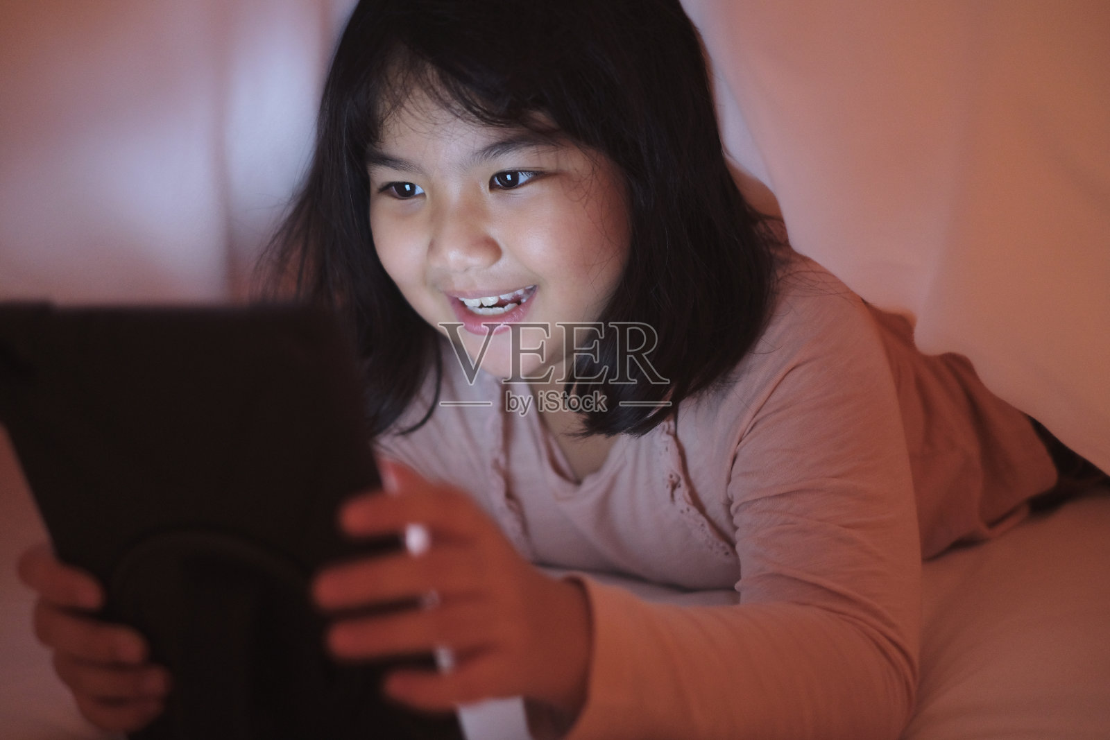 在被子下使用平板电脑的可爱小女孩照片摄影图片