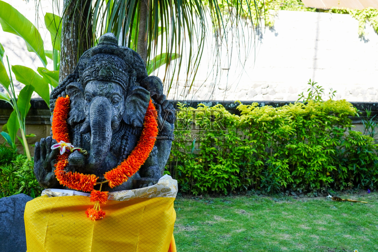 头戴黄色花环的甘尼萨神雕像，这是印度教巴厘岛宗教信仰的传统照片摄影图片