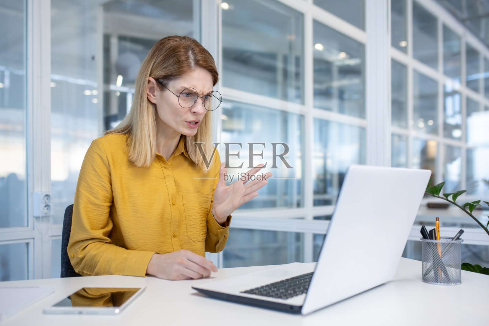 穿着黄色衬衫的女商人在现代办公室的视频会议中使用笔记本电脑照片摄影图片