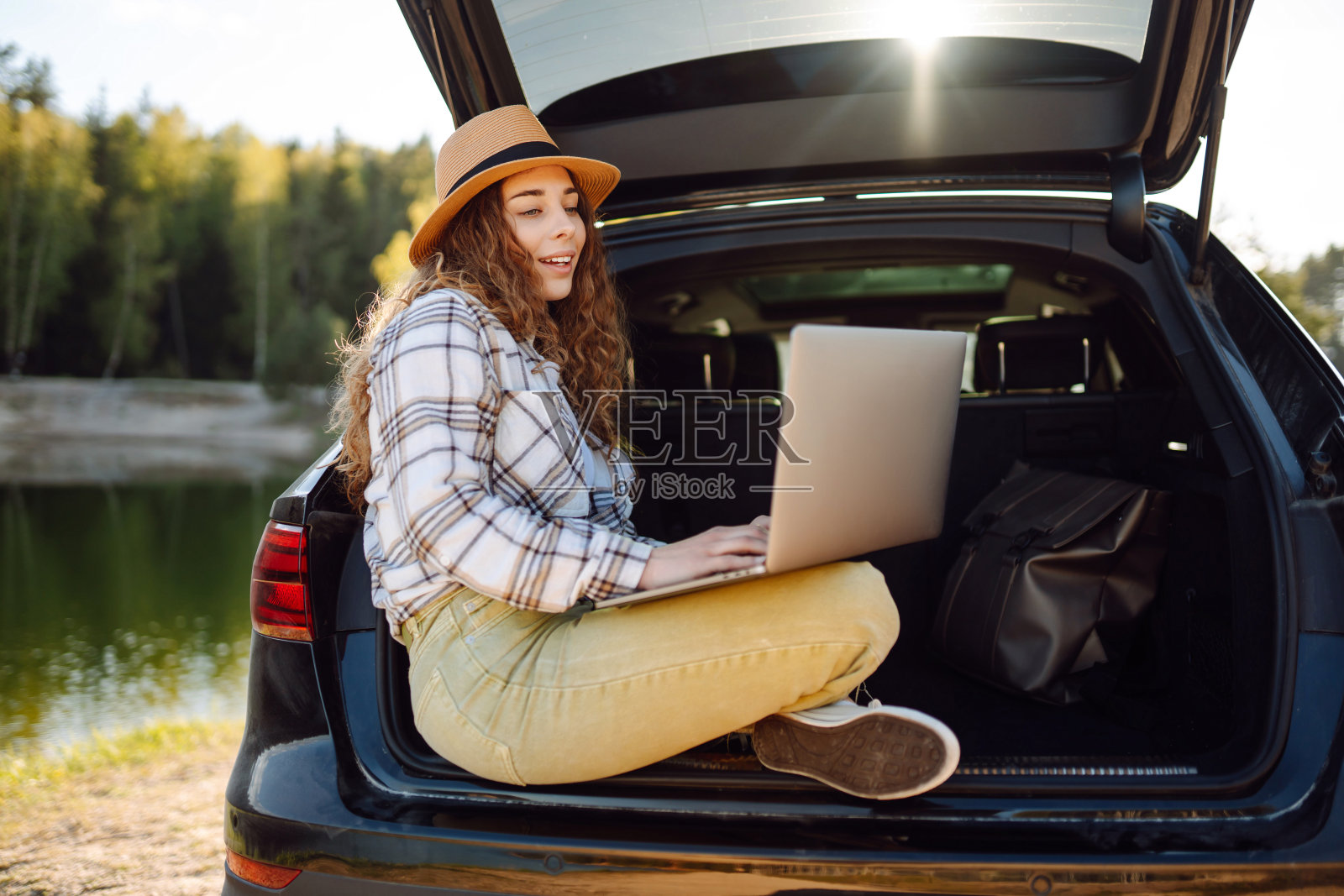 年轻女子坐在汽车后备箱里使用笔记本电脑。照片摄影图片