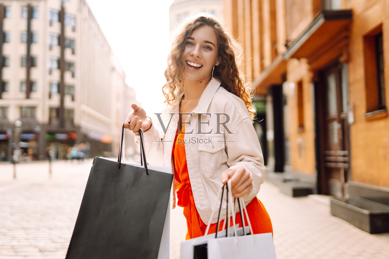 年轻漂亮的女人拿着买的东西走出商场。照片摄影图片