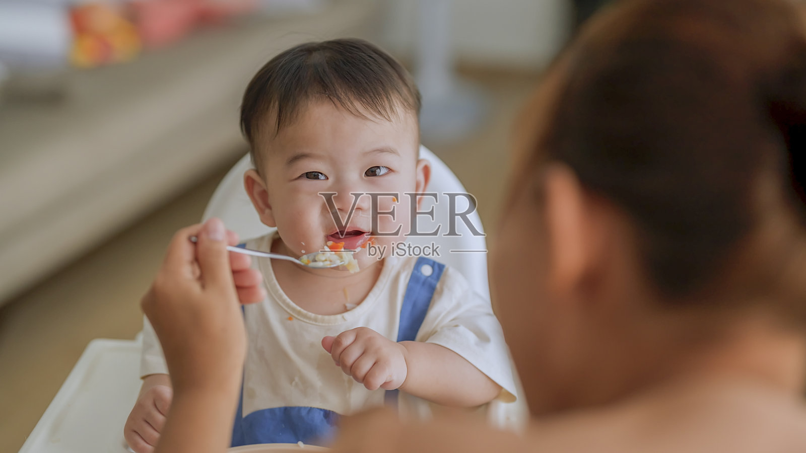 亚洲妈妈在家用高脚椅上用勺子喂凌乱的女婴的照片宝宝里程碑，成长和发展的概念照片摄影图片