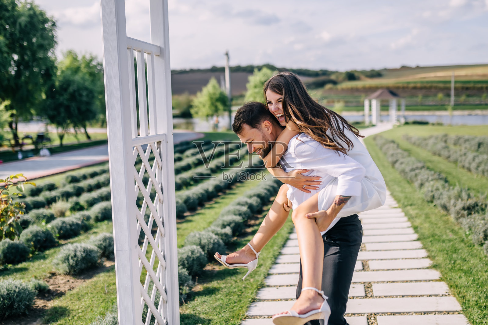 婚礼结束后，一对兴高采烈的夫妇在绿油油的花园里散步，在小巷两旁的灌木丛中开心地玩耍。一个男人和一个背着ai的女人鬼混。照片摄影图片