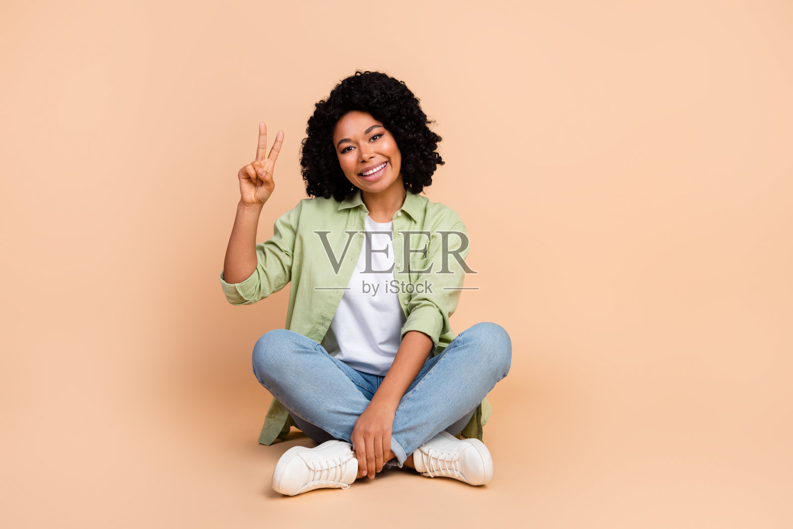 漂亮的年轻女士的全尺寸照片，坐在地板上，穿着米色背景上的v字衬衫照片摄影图片