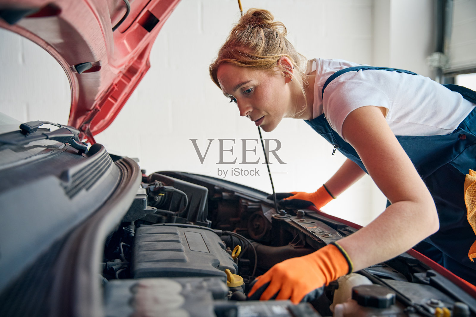 一位女汽车修理工正在检查正在维修的汽车引擎盖下的发动机照片摄影图片