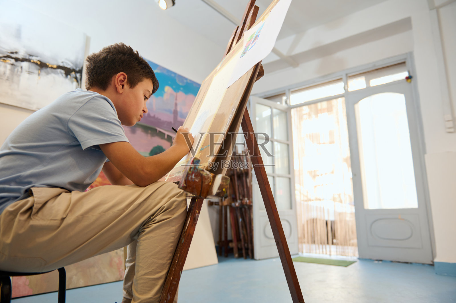 美术课上，小男孩在画架上画画照片摄影图片