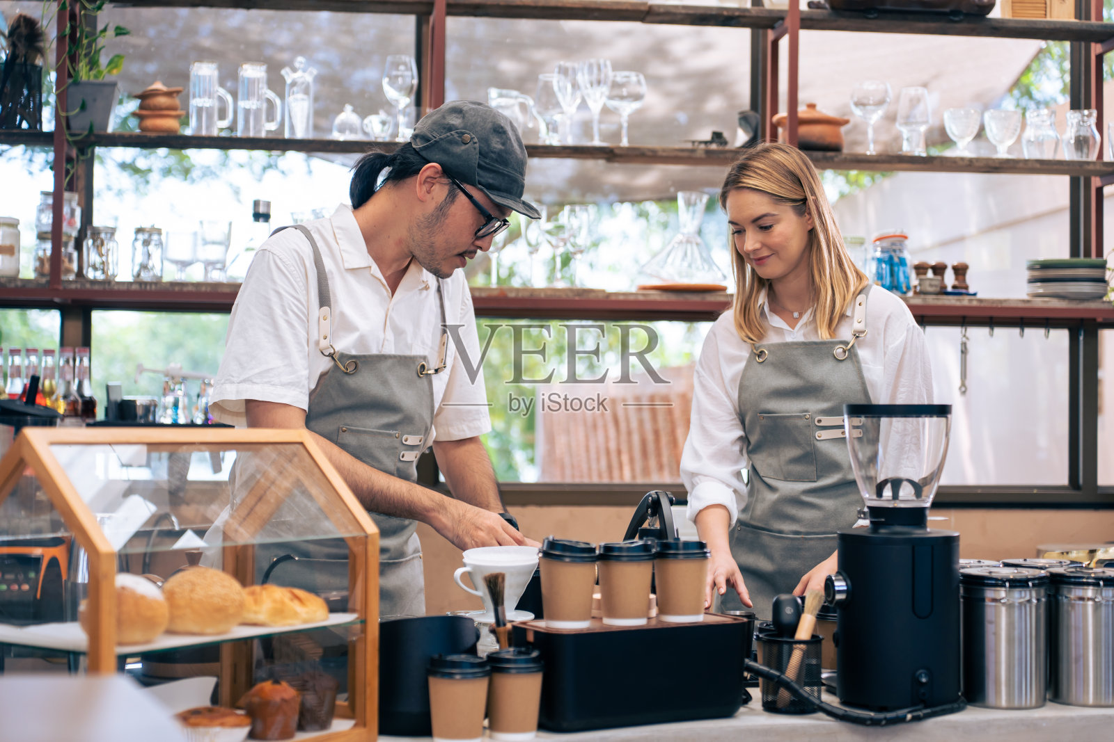 亚洲帅哥男咖啡师和女服务员在咖啡馆工作。年轻英俊的企业家，系着围裙，教女服务员在城市餐厅的柜台上磨咖啡豆煮咖啡照片摄影图片