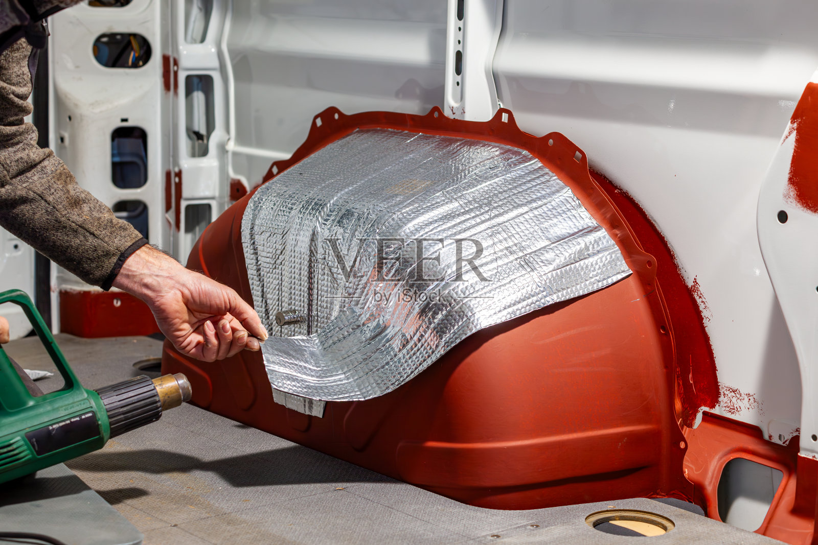 DIY露营车跳车转换。铝丁基垫。使用热风枪的人。房车内的隔音胶垫。小车，泡沫隔热效果好，吸音。噪音保护照片摄影图片