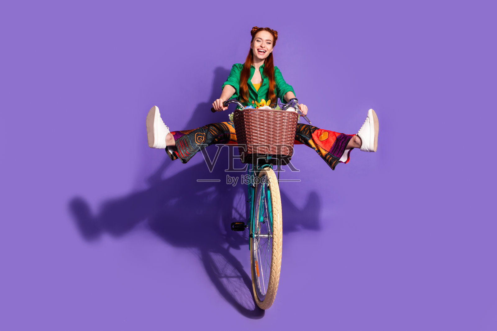全尺寸照片，疯狂的无忧无虑的女人穿着绿色的衬衫，复古的裤子，抱着腿骑自行车孤立的紫色背景照片摄影图片