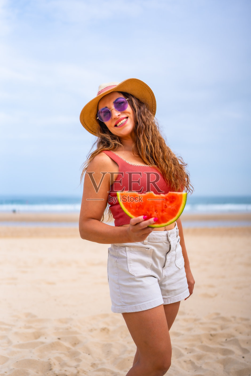 在海滩度假，戴着帽子抱着西瓜享受夏日的白人女性照片摄影图片