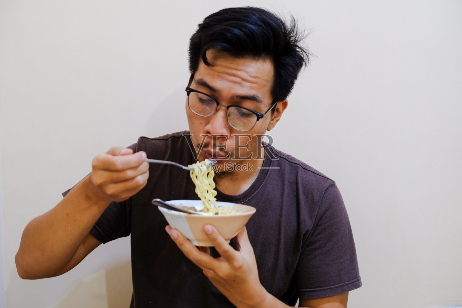 一名东南亚男子拿着白碗里的面条吃照片摄影图片