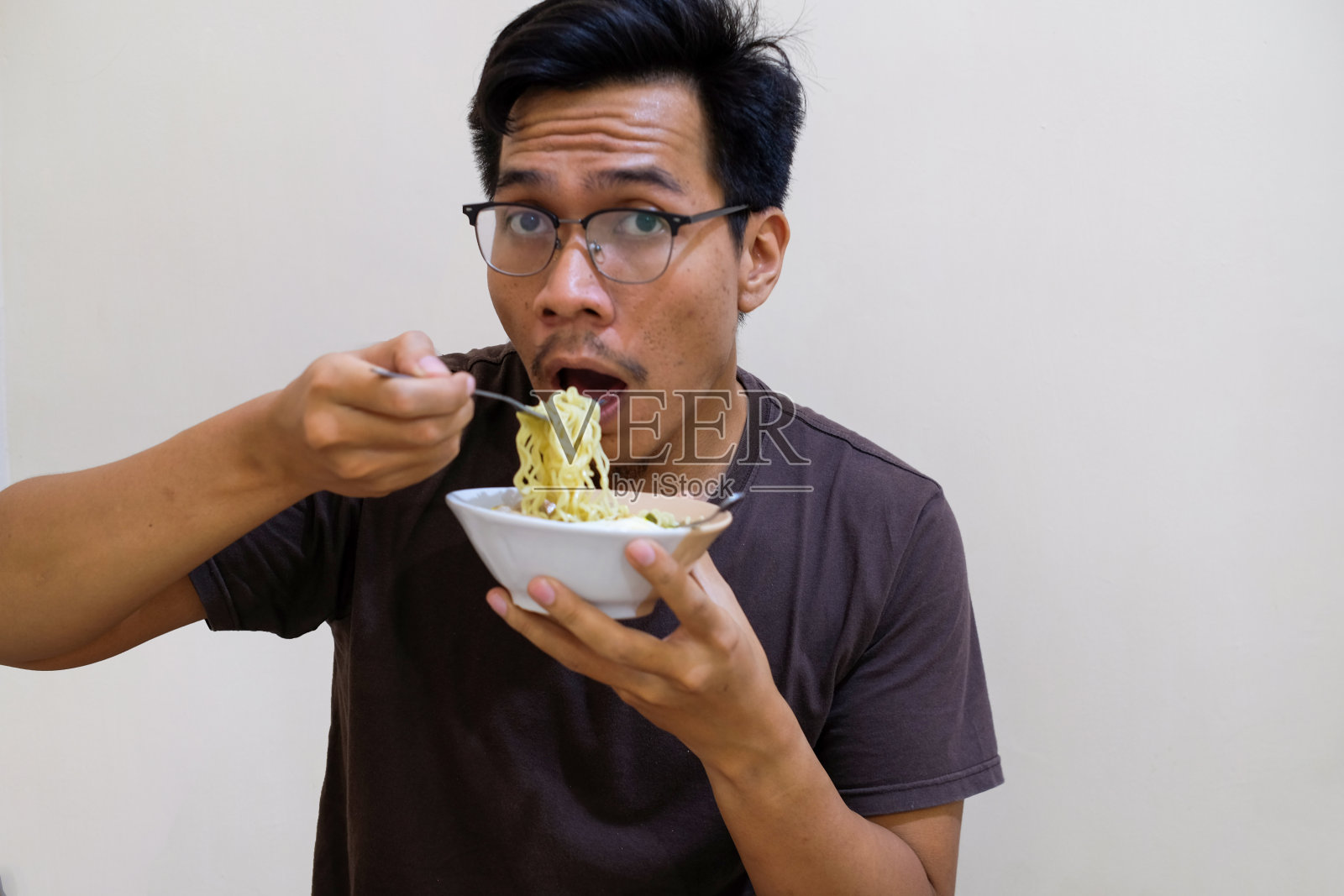 一名东南亚男子拿着白碗里的面条吃照片摄影图片