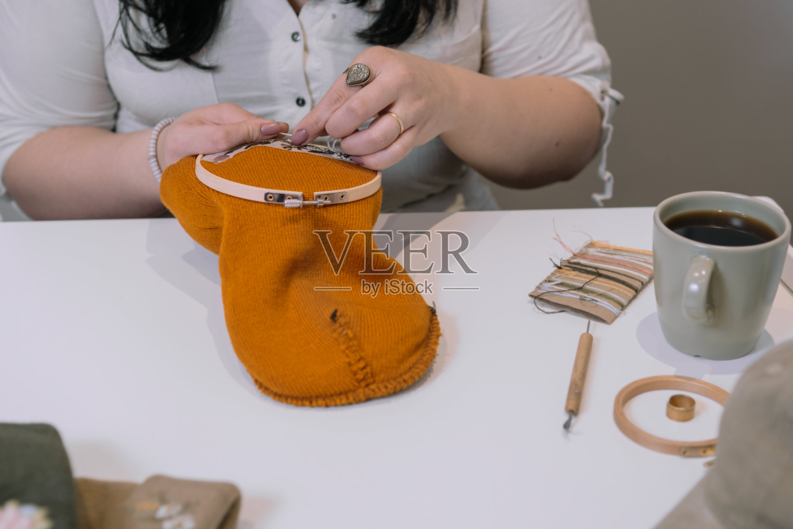 一个女人坐在桌子旁，手里拿着一台缝纫机和一杯咖啡照片摄影图片