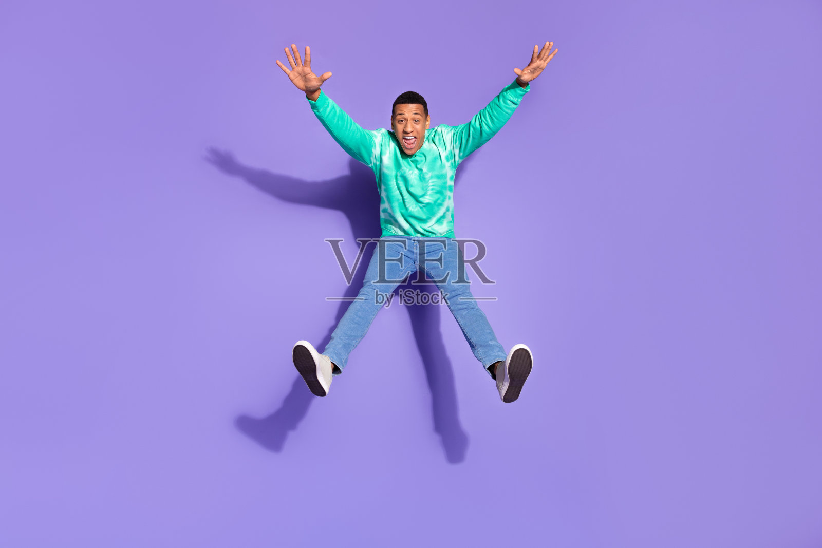 时髦酷的家伙穿着绿松石运动衫跳得很高，像星星一样空旷的空间孤立的紫罗兰色背景照片摄影图片