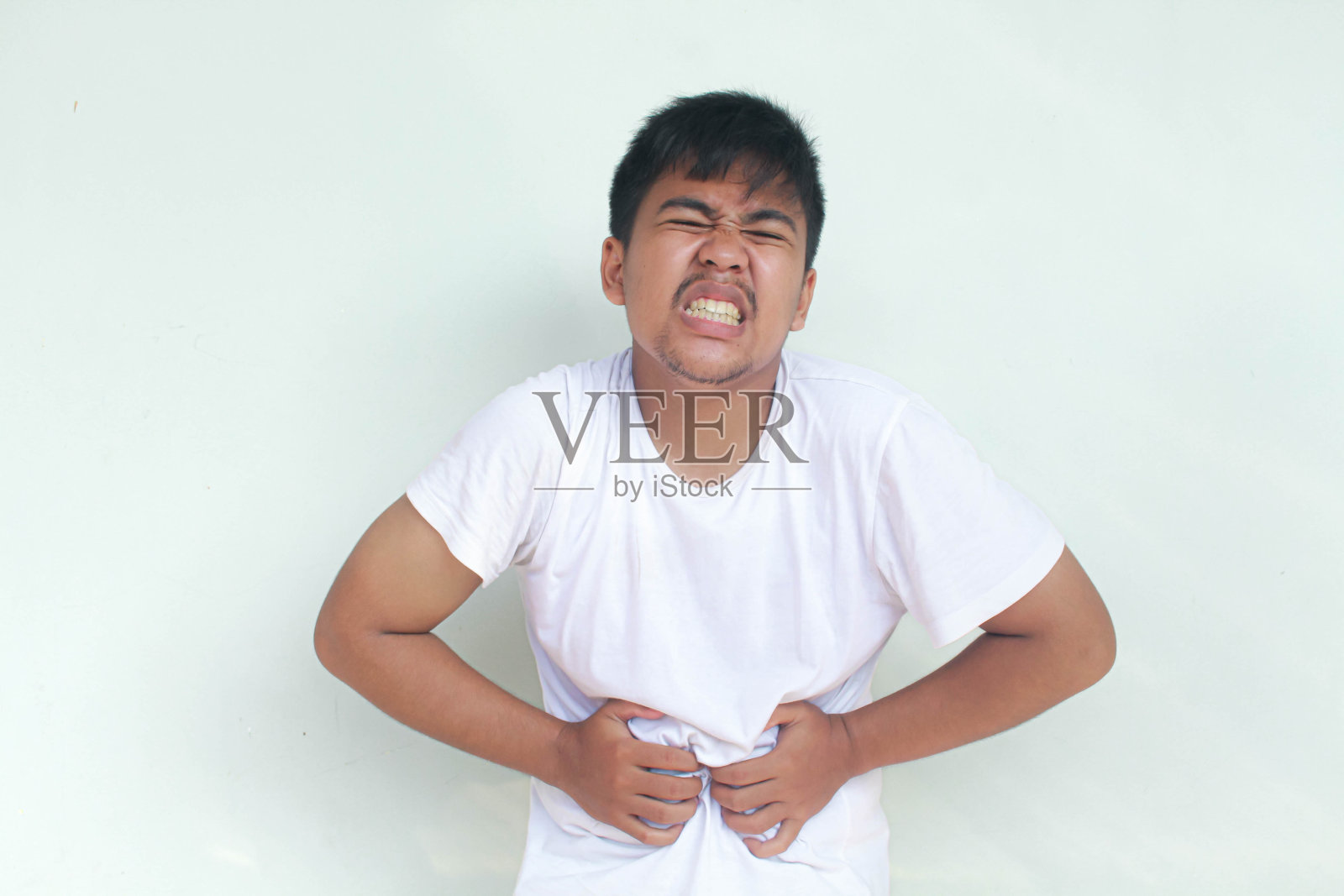 穿着便服的年轻亚洲男子捂着肚子，感到疼痛。照片摄影图片