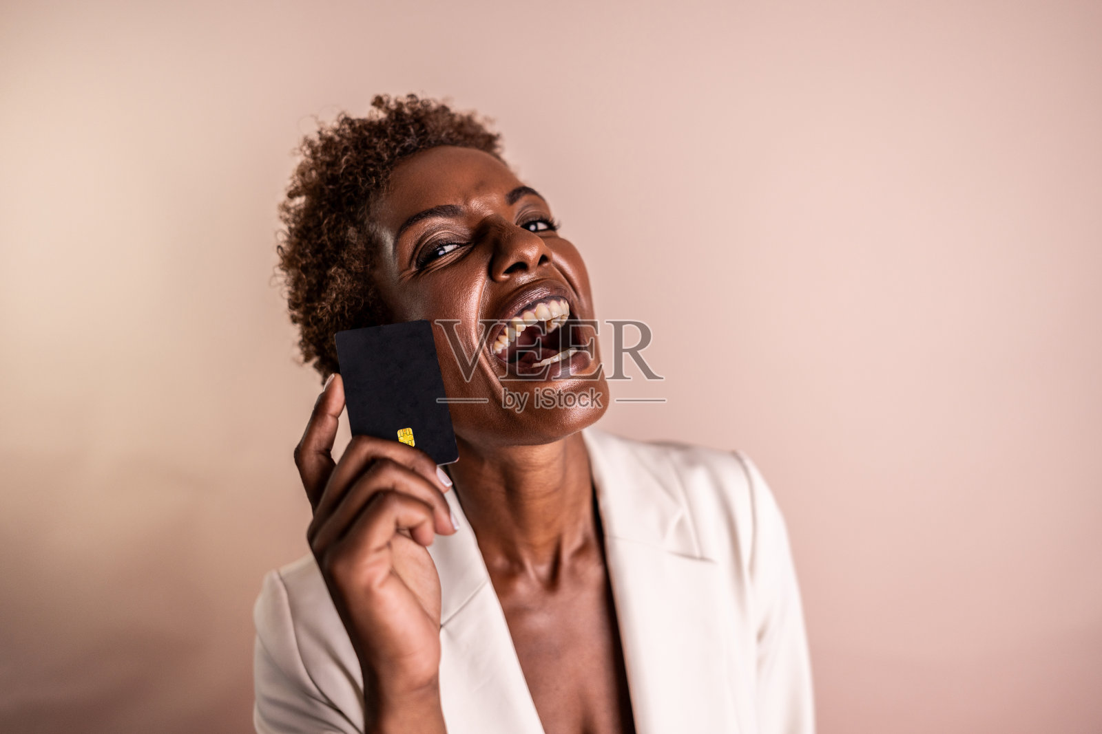 成熟的女商人手持黑色信用卡的肖像，在摄影棚拍摄，背景为奶油色照片摄影图片