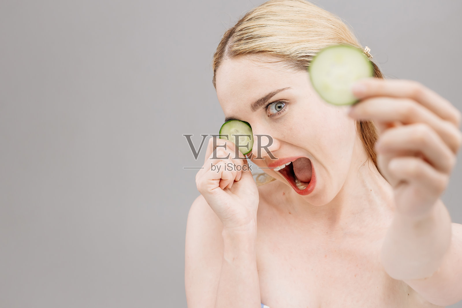 一位年轻美丽的金发女郎用新鲜黄瓜片敷眼。皮肤护理和治疗，水疗，自然美容和美容照片摄影图片