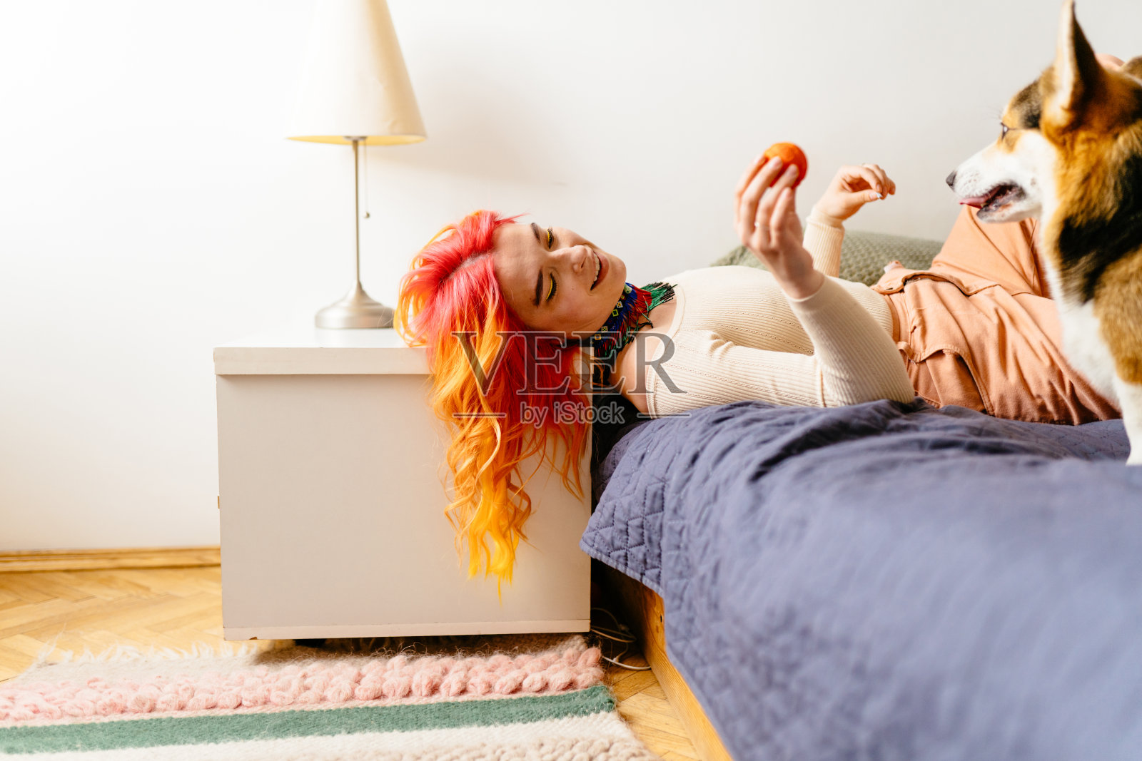 一个橙色头发的女人躺在床上，旁边是一只狗。狗嘴里衔着一个橘子照片摄影图片