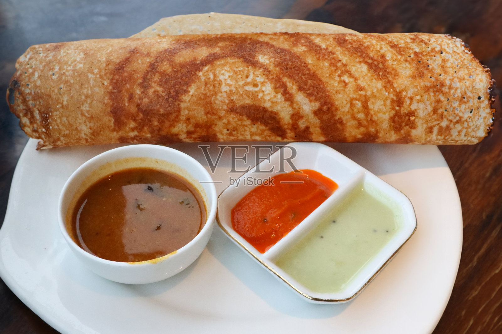 白色盘子里的特写图片，里面装着马萨拉土豆泥和切碎的洋葱，里面塞满了马萨拉土豆泥，还有调味料、椰子酸辣酱和桑巴，早餐时间，木纹背景，提升视野照片摄影图片