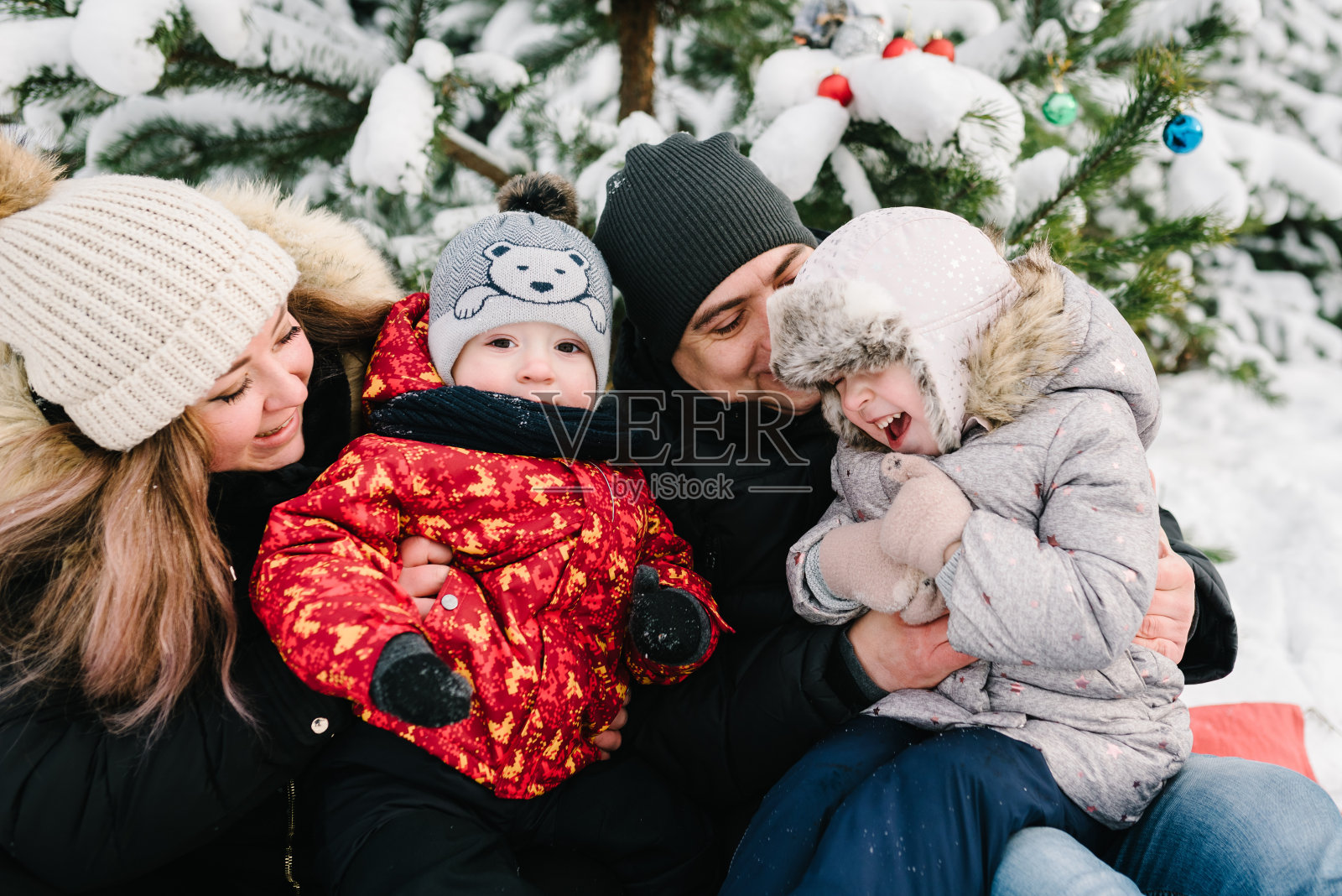 父亲，母亲，孩子走山，时间在一起。冬天的假期。幸福的一家人在公园里散步，旁边是白雪装饰的圣诞树。妈妈、爸爸、儿子、女儿坐在冬天森林里的雪地里。照片摄影图片