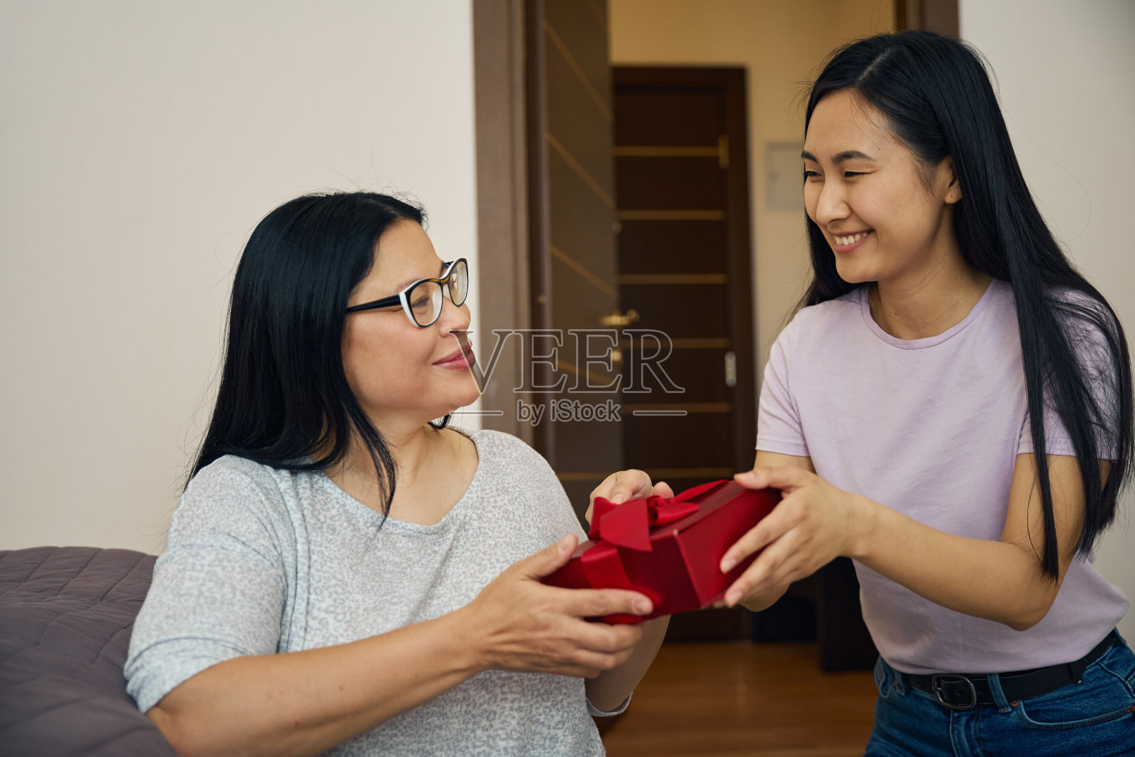 在卧室里，微笑的女儿给心满意足的母亲送礼物照片摄影图片