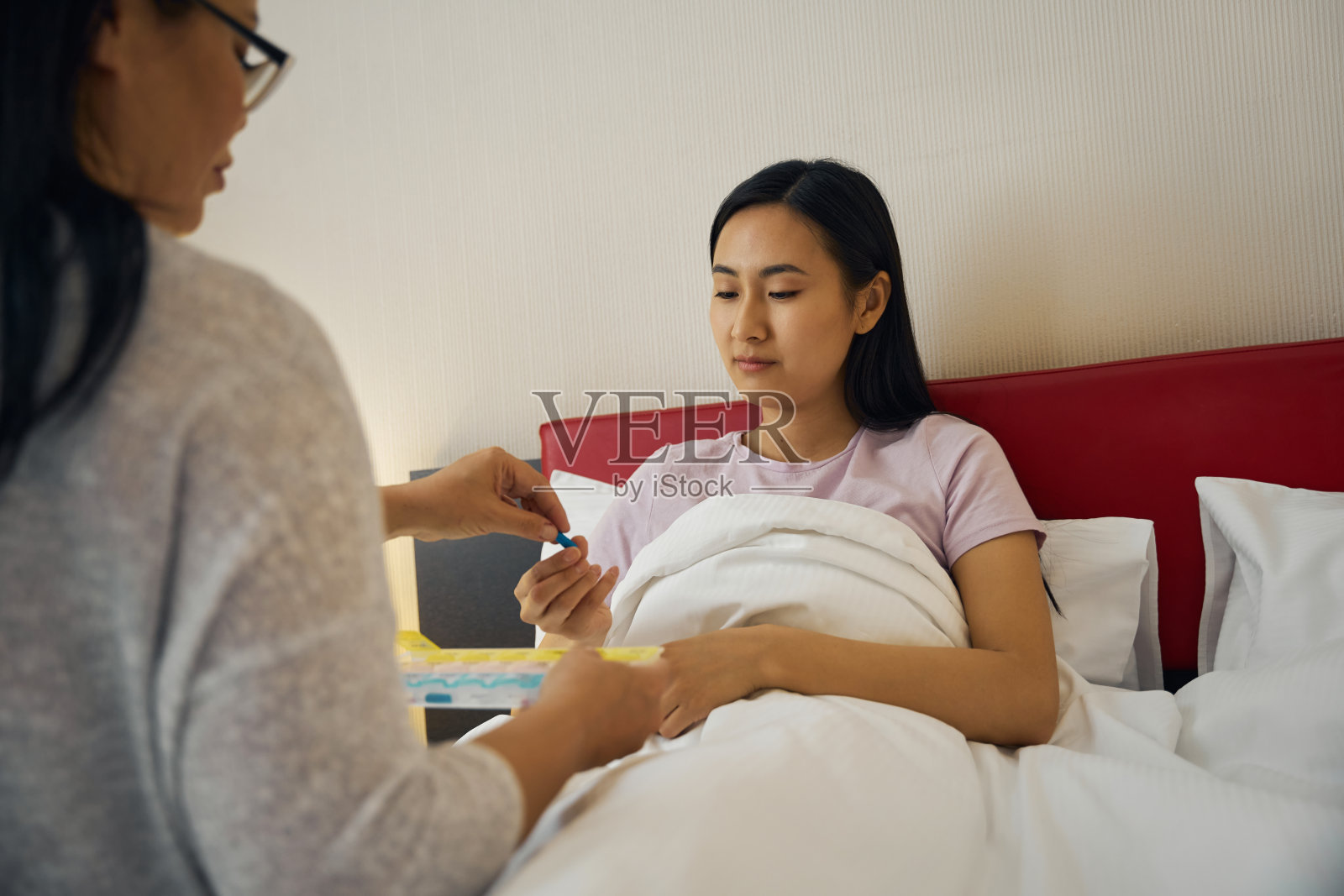 慈爱的母亲在卧室里给生病的成年女儿喂药照片摄影图片